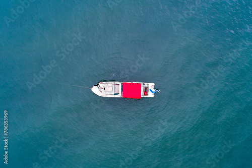 Top-down view of a small fishing boat with a bright red canopy on a vast expanse of blue water