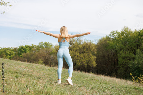 Athlete practicing in the park doing squats on one leg me her. Beautiful blonde Caucasian woman in blue tight tracksuit. Blonde girl at an outdoor training session