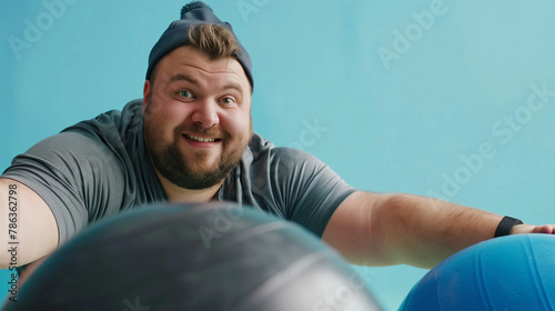 Playful body positive man with a headband exercising with a fitness ball photo