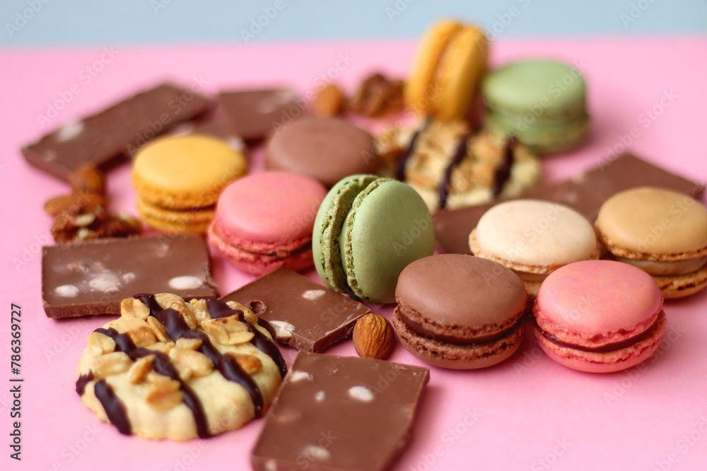 Pastel macarons, almond chocolate, peanut butter cookies and various nuts on bright pink background. Selective focus. Pastel macarons, almond chocolate, peanut butter cookies and various nuts on bright pink background. Selective focus.