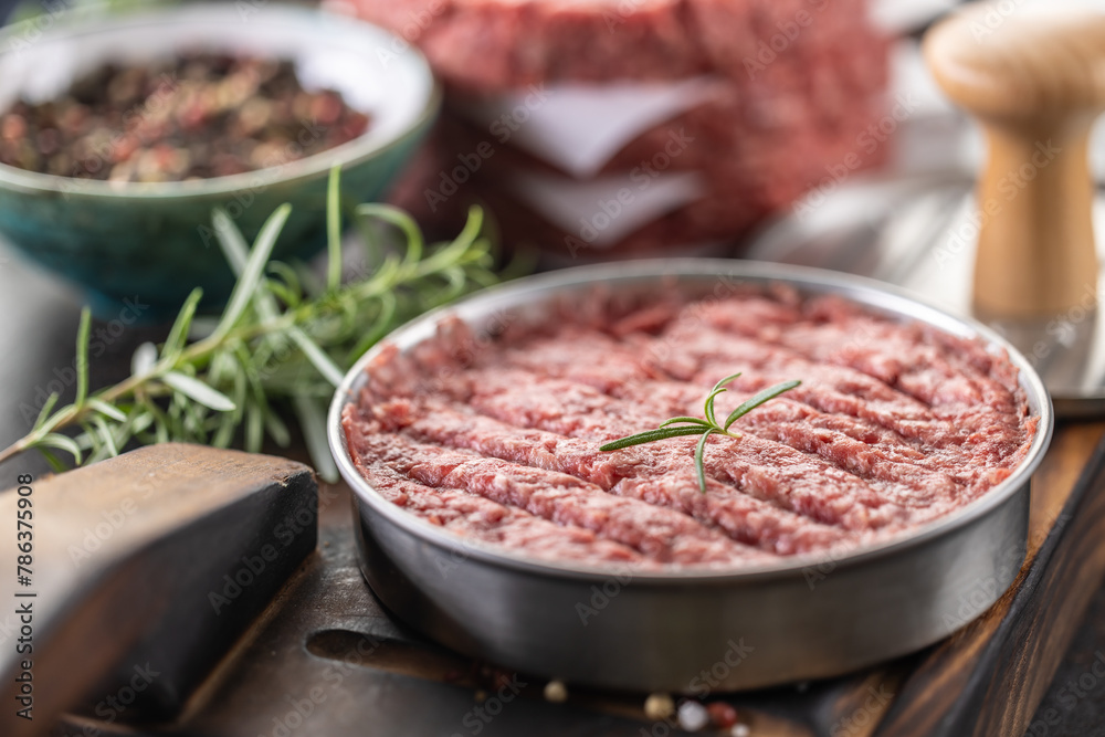 Fresh raw ground beef patties with rosemary salt and pepper made in a meat form on a cutting board Fresh raw ground beef patties with rosemary salt and pepper made in a meat form on a cutting board