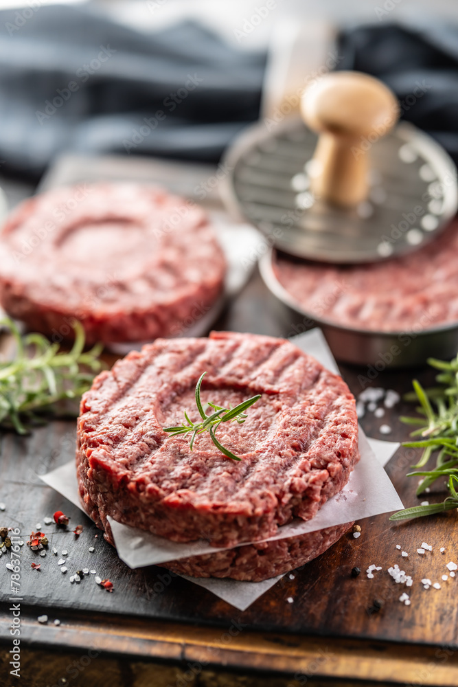 Fresh raw ground beef patties with rosemary salt and pepper made in a meat form on a cutting board Fresh raw ground beef patties with rosemary salt and pepper made in a meat form on a cutting board