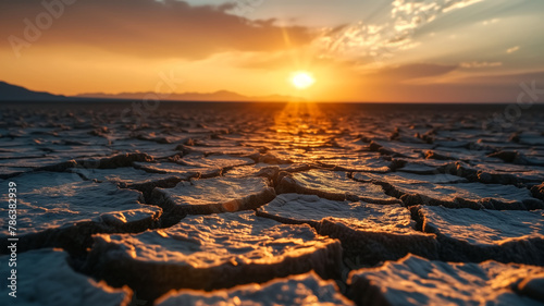 Sunset over cracked desert floor. Dramatic landscape with sun flare and warm tones. Climate change and drought concept. Close-up ground perspective with horizon. 