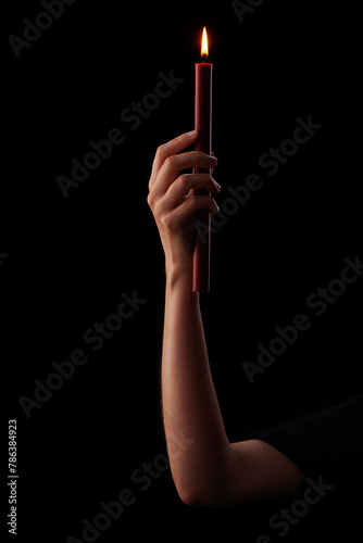 Woman’s hand holding red wax candle burning brightly on black