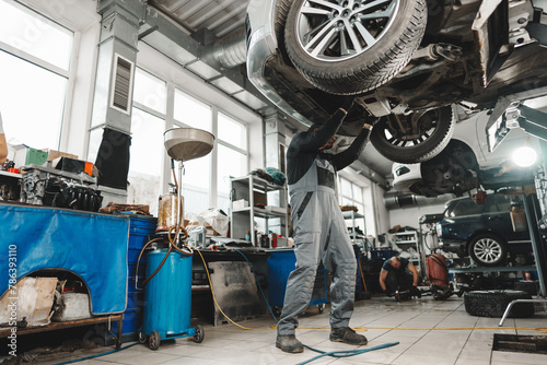 Workman mechanic working under car in auto repair shop photo