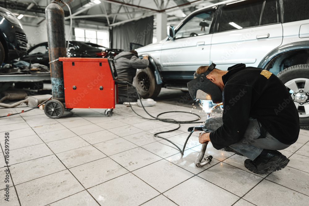 Fototapeta premium Welder in mask repairing detail in car service