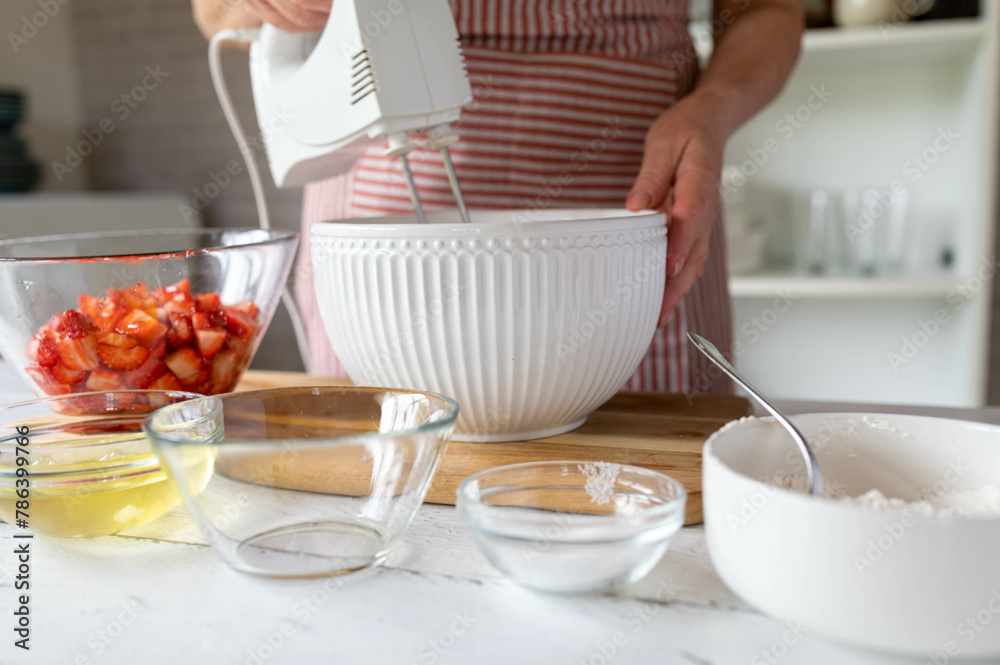 Woman mixing dough or batter  with a hand mixer for making a strawberry cake