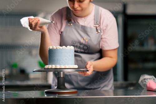Fototapeta Naklejka Na Ścianę i Meble -  of a female baker in a professional kitchen decorating a blue cake with cream