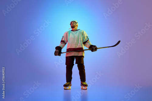 Photography Motivated and ambitions man, hockey player in uniform standing with confident look against gradient blue background in neon light