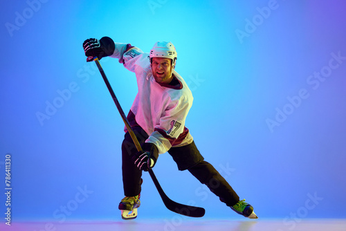 Photography Competitive, motivated man, hockey player posing with stick, in uniform and helmet against gradient blue background in neon light