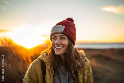 Portrait of a cheerful woman in her 30s sporting a trendy beanie in front of vibrant sunset horizon © Markus Schröder