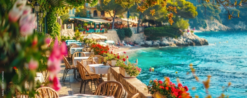 Authentic atmospheric cafe on the shore of the French Riviera under green trees overlooking clear blue water, colorful flowers in the background - obrazy, fototapety, plakaty 