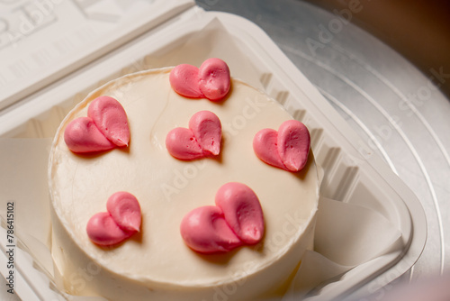 close-up in a white box of a finished small white cake with pink cream hearts
