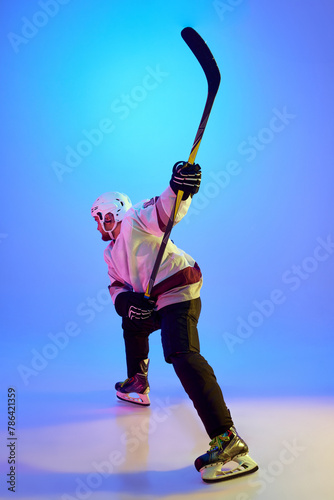 Canvas Print Ambitious man, hockey player posing with stick, showing his determination against gradient blue background in neon light
