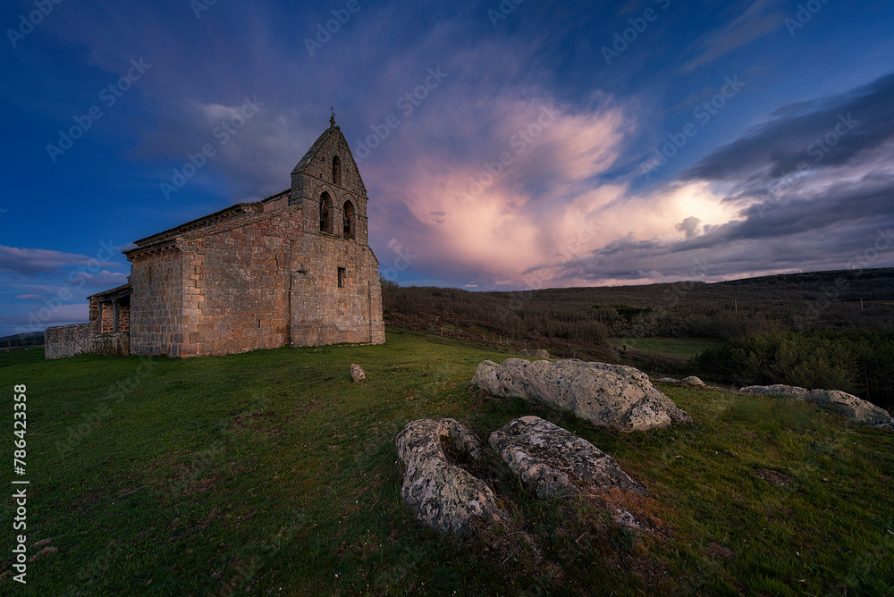 Sunset with dramatic sky in the Romanesque church of San Martín, in Quintanilla de la Berzosa, Aguilar de Campoo, Palencia, Castilla y León, with the tombs of the medieval necropolis in the foreground