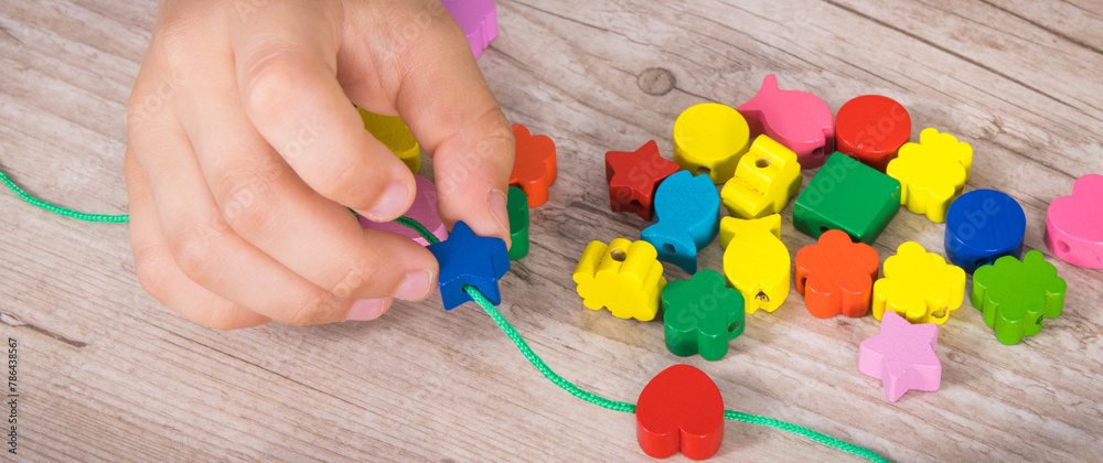 Preschooler making bracelet from thread and wooden colored beads ...