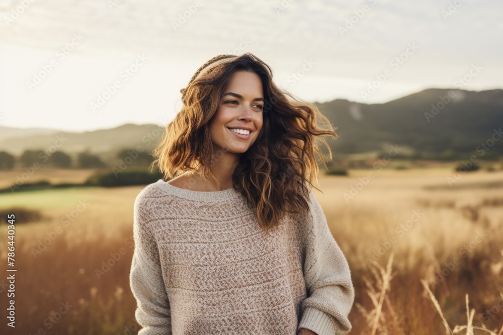 Portrait of a happy woman in her 30s wearing a cozy sweater over quiet countryside landscape Portrait of a happy woman in her 30s wearing a cozy sweater over quiet countryside landscape