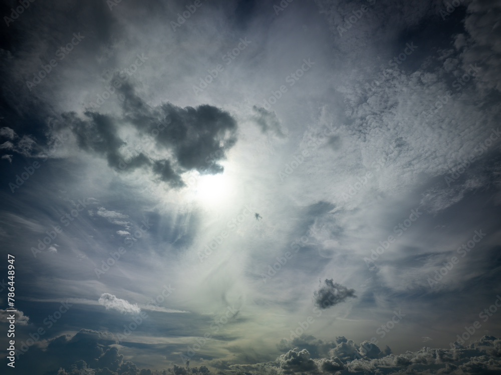 A dramatic sky filled with various types of clouds, with the sun shining brightly through, creating a beautiful light effect.