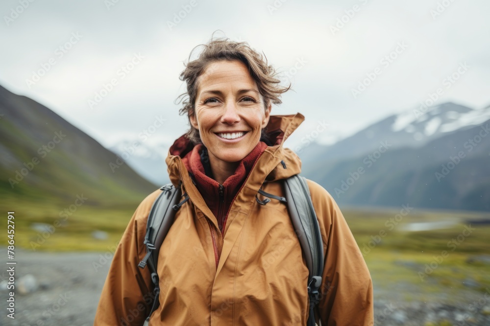 Portrait of a joyful woman in her 40s wearing a lightweight packable anorak isolated on backdrop of mountain peaks