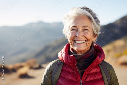 Portrait of a smiling woman in her 70s wearing a thermal fleece pullover isolated on backdrop of mountain peaks