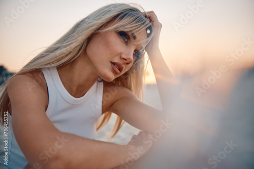 A contemplative woman holds her hair against a stunning ocean sunset on a peaceful beach setting
