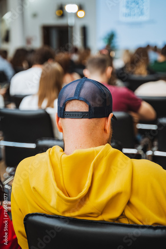 Man in yellow hoodie and blue hat sits in front of crowd at a competition event © Aleksey