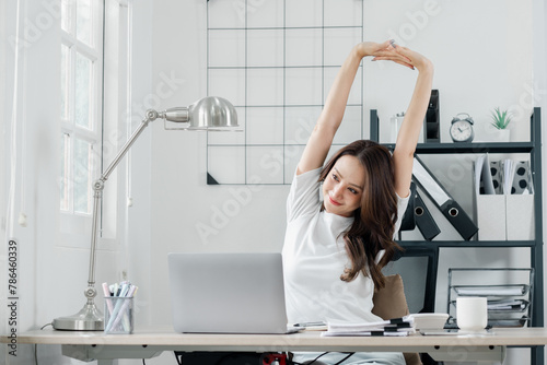 Businesswoman takes a moment to stretch and relax at her desk  in a bright and airy office space.