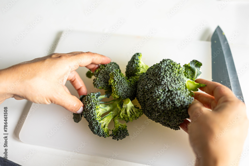 A girl cuts broccoli for soup. Sliced broccoli on a cutting board. A woman is preparing broccoli.