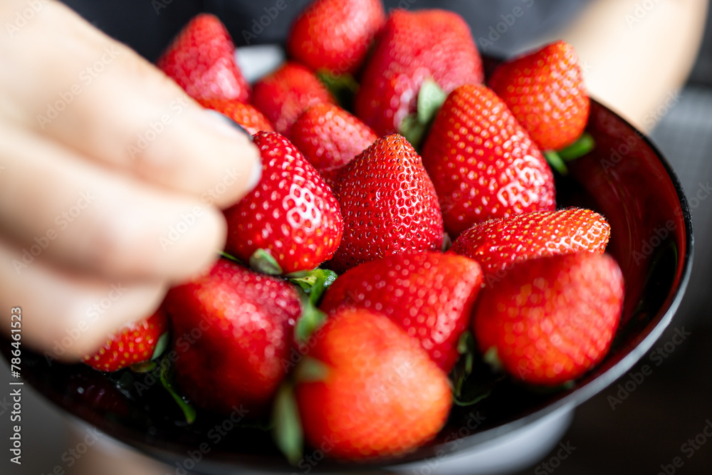 Juicy, sweet, ripe, fresh strawberries in a plate. A handful of strawberries in a saucer. The girl takes a strawberry with her hand.