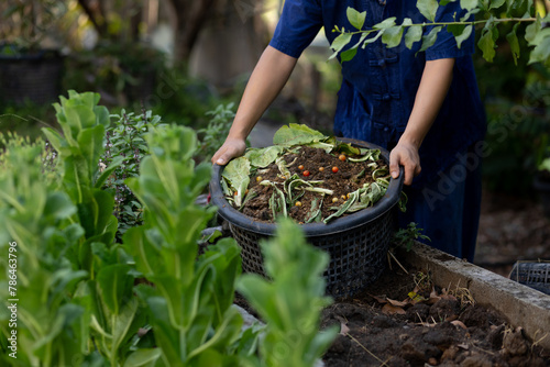 Farmer composts food waste into soil in lush green farm garden.