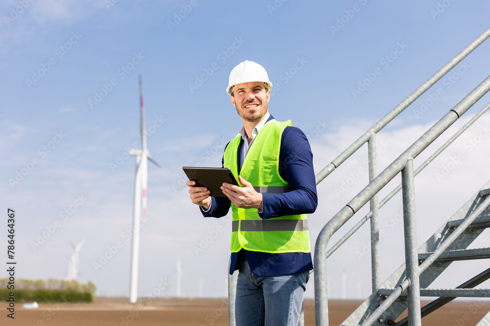 Smiling Engineer With Tablet Inspecting Wind Turbines On A Sunny Day Smiling Engineer With Tablet Inspecting Wind Turbines On A Sunny Day