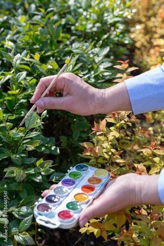 A blurry image of a girl’s hand with a brush painting green leaves on the street.