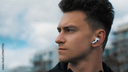 Portrait of a young confident man. Listens to music in headphones. In the city park