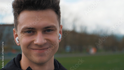 Portrait of a young smiling man. The man is looking at the camera. With headphones headphones. Listens to music in headphones