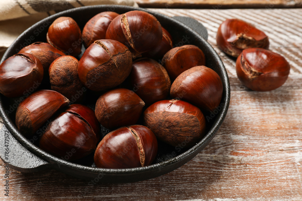 Fresh edible sweet chestnuts in frying pan on wooden table, closeup Fresh edible sweet chestnuts in frying pan on wooden table, closeup