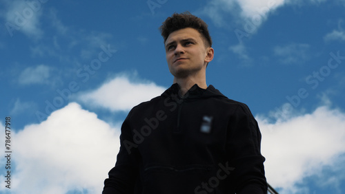Confident young man standing against the background of the blue sky.