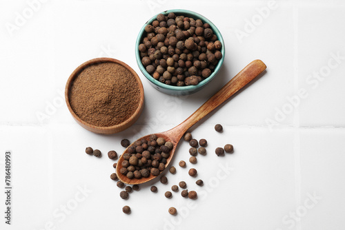 Ground and whole allspice berries (Jamaica pepper) on white tiled table, flat lay