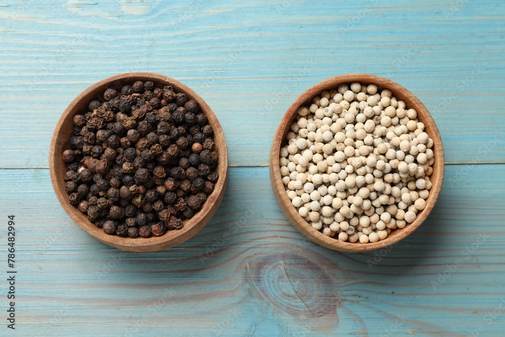 Aromatic spice. White and black peppers in bowls on light blue wooden table, top view Aromatic spice. White and black peppers in bowls on light blue wooden table, top view