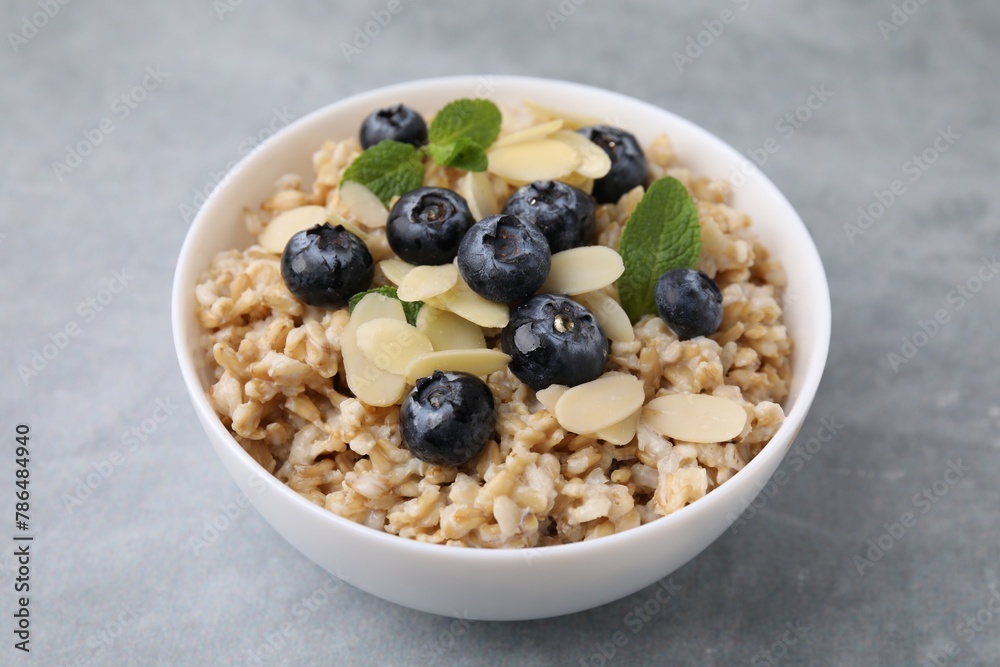 Tasty oatmeal with blueberries, mint and almond petals in bowl on grey table Tasty oatmeal with blueberries, mint and almond petals in bowl on grey table