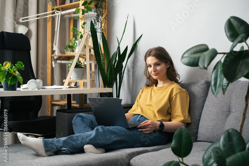 Beautiful young woman talking on video chat or working remotely from her cosy home garden surrounded by plants.