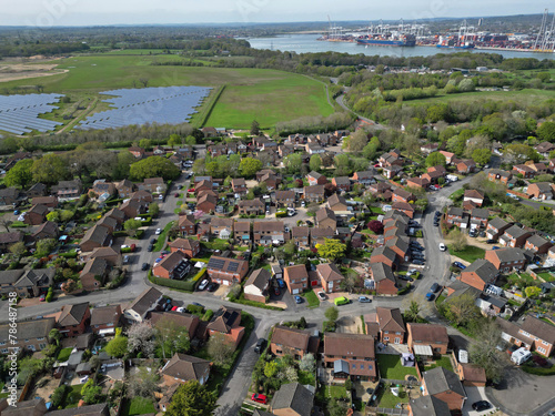 Aerial view of Marchwood residential street with houses and solar farm towards Southampton docks, UK. Southampton container terminal and container ships.