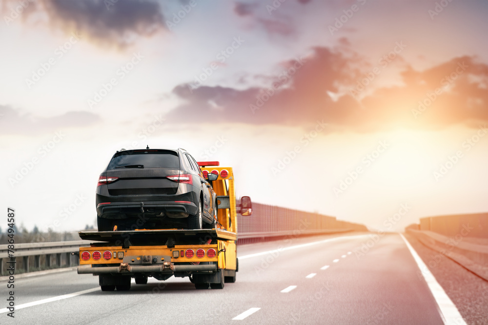 Roadside assistance. Tow truck transporting a broken car on a highway. Flatbed towing truck with a car on the road. Car service transportation concept.