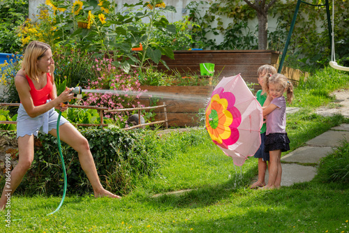 Summer day garden fun play of kids and mother with water hose