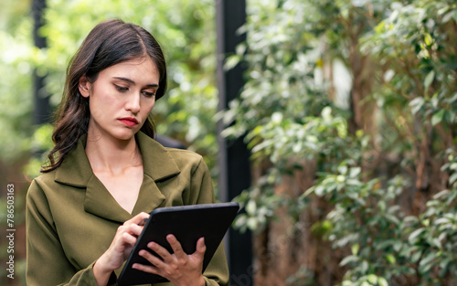 Caucasian beautiful smart businesswoman wearing formal clothes, holding, using tablet, standing outdoor in morning, thinking, professional working, making serious face. Business Concept.