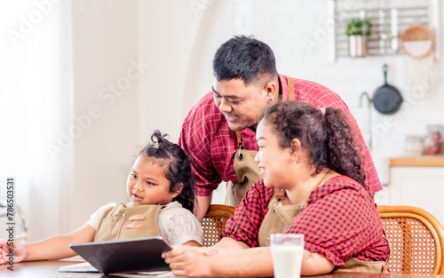 Asian parent wearing casual clothes, teaching daughter to do homework at home, drinking milk, smiling with warmth and happiness. Family, Education Concept.