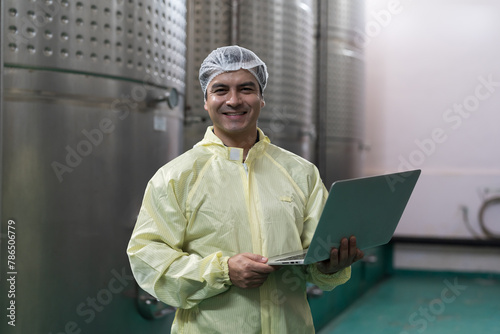 Winemaker inspecting quality the process of fermentation during manufacturing in winery factory and stainless tank. Male winemaker working with laptop computer in winery factory