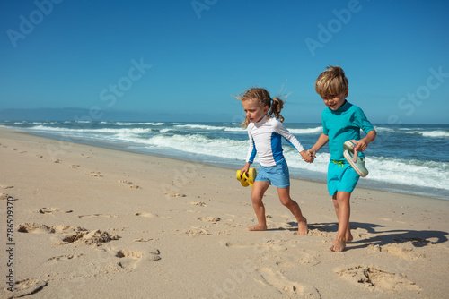 Siblings, boy and girl, hold hands walk barefoot on sandy shore