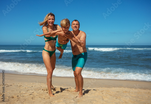 Parents play with child on sunny beach, hold him in arms, swing
