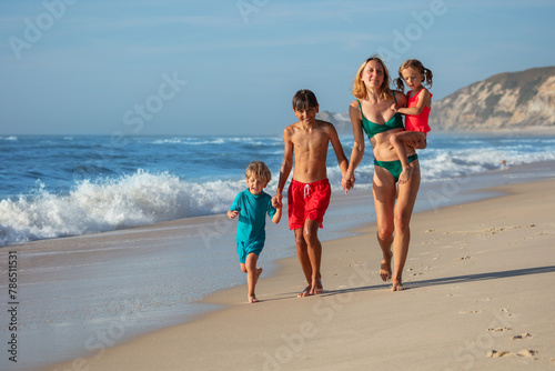 Woman and two kids, dressed for swim, have fun run on sand beach