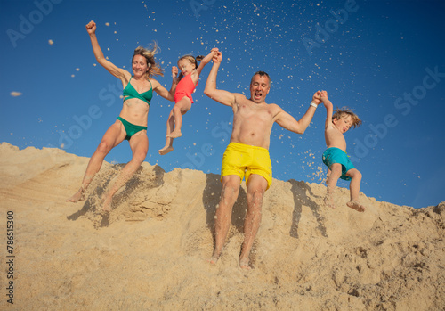 A joyful family leaping from sandy ridge against clear blue sky